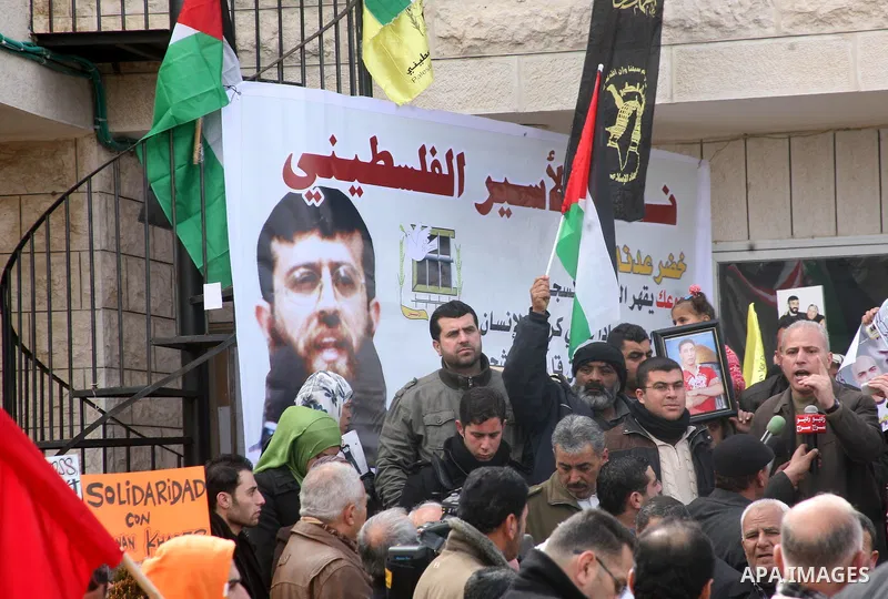 Palestinians holds a portrait of Khader Adnan, a Palestinian held in an Israeli prison without trial and who is on hunger strike since December 18, during a protest in front of the Red Cross office in the West Bank city...