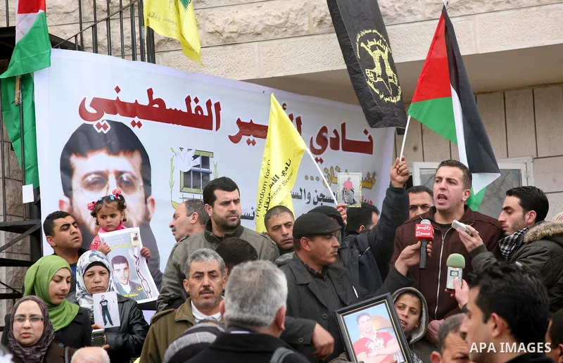 Palestinians holds a portrait of Khader Adnan, a Palestinian held in an Israeli prison without trial and who is on hunger strike since December 18, during a protest in front of the Red Cross office in the West Bank city...