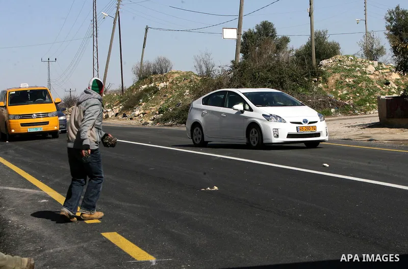 Palestinian youth throw stones at a vehicle driven by an Israeli settler along Route 60 to a Jewish settlement which passes close to the village of Beit Omar in the Israeli occupied West Bank, on February 21, 2012. Stone...