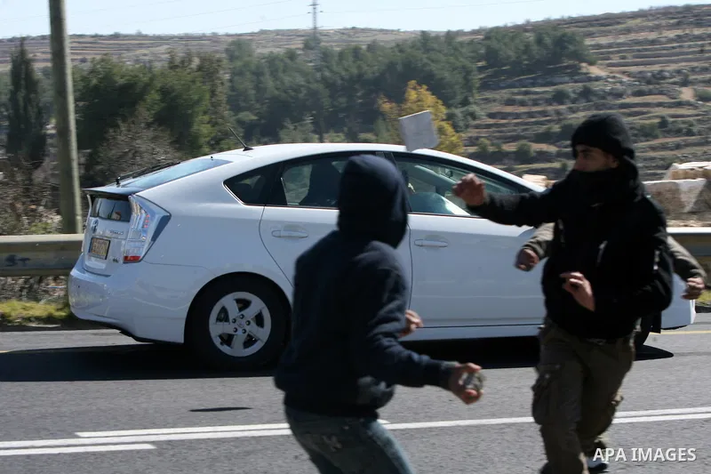 Palestinian youth throw stones at a vehicle driven by an Israeli settler along Route 60 to a Jewish settlement which passes close to the village of Beit Omar in the Israeli occupied West Bank, on February 21, 2012. Stone...