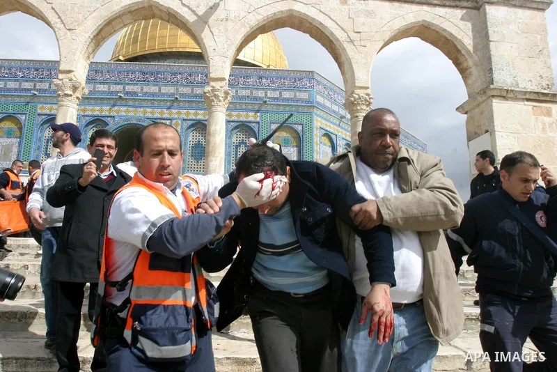 A Palestinian medic and a civilian assist a Palestinian man bleeding from his head as they remove him from near the Dome of the Rock, behind, during running clashes between Palestinians and Israeli policemen on the compo...