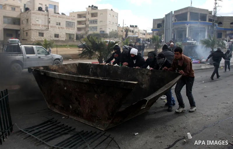 Masked Palestinian protesters run away from tear gas fired by Israeli security forces, not pictured, during clashes in the West Bank town of Al-Ram, near Jerusalem, Saturday, Feb. 25, 2012. Clashes erupted after the fune...