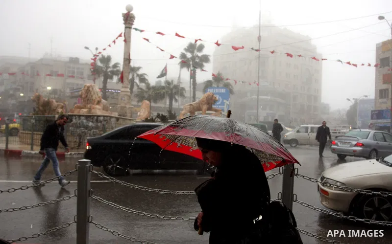 Palestinians walk in a street during the heavy rain and cold winds in the West Bank city of Ramallah on 29 Feb, 2012. Photo by Issam Rimawi