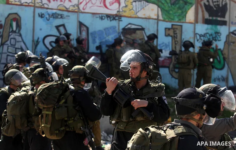 Israeli soldiers standing before the separation wall, protect themselves against teargas during a protest next to the checkpoint of Kalandia, West Bank, 08 March 2012, North of Jerusalem, during a rally to mark the Inter...
