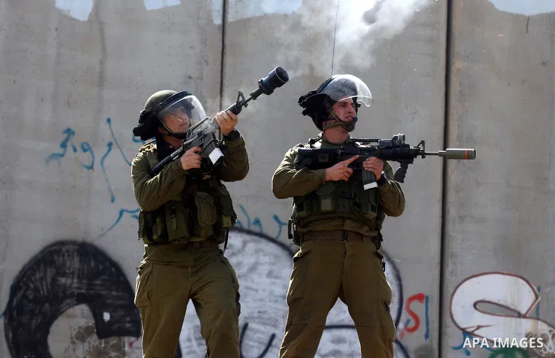 Israeli soldiers standing before the separation wall, protect themselves against teargas during a protest next to the checkpoint of Kalandia, West Bank, 08 March 2012, North of Jerusalem, during a rally to mark the Inter...