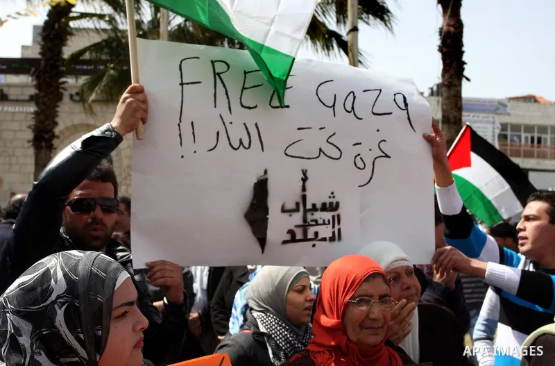 A Palestinian woman shouts slogans during a rally in support of Palestinians in Gaza Strip in the West Bank city of Ramallah, Sunday, March. 11, 2012. The Arabic text on the banner reads: g "Free Gaza, Gaza under fire"....