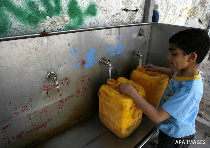 Palestinian children filling plastic bottles and jerry cans with drinking water from a public tap at the United Nations Relief and Works Agency (UNRWA) headquarters in the southern Gaza Strip refugee camp of Rafah on Mar...