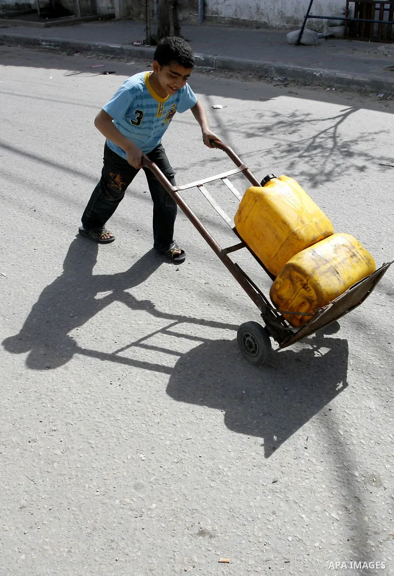 Palestinian children filling plastic bottles and jerry cans with drinking water from a public tap at the United Nations Relief and Works Agency (UNRWA) headquarters in the southern Gaza Strip refugee camp of Rafah on Mar...