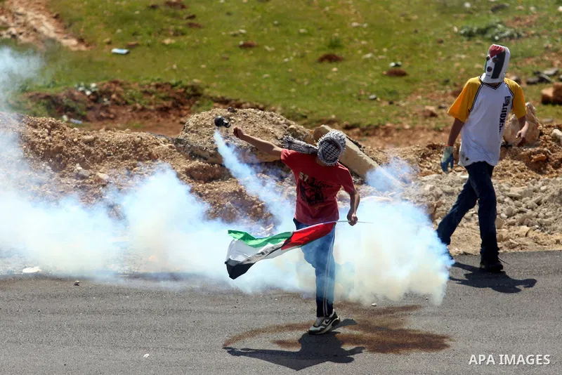 A Palestinian demonstrator returns a tear gas canister towards Israeli soldiers during a protest against the expansion of the nearby Jewish settlement of Halamish in the West Bank village of Nabi Saleh near Ramallah, Fri...