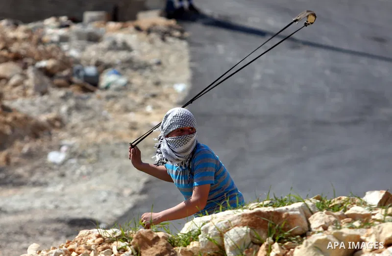 A Palestinian protester swings a sling at Israeli troops during a protest against the expansion of the nearby Jewish settlement of Halamish in the West Bank village of Nabi Saleh, near Ramallah, Friday, March 23, 2012. P...