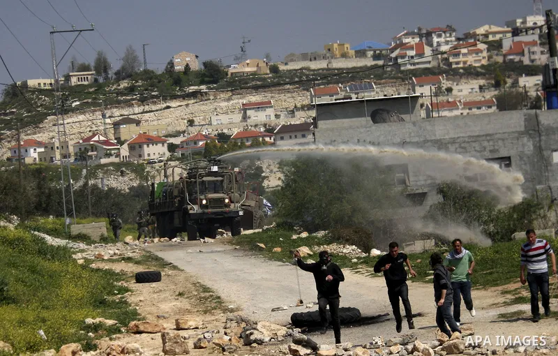 Palestinian protesters run away from a Israeli military vehicle spraying foul smelling water during clashes at a demonstration against the closure of a road for Palestinians in the West Bank village of Kfar Kadum, near N...
