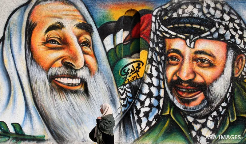 palestinians walk near of the mural of late Palestinian leader Yasser Arafat and late Hamas leader Sheikh Ahmed Yassin , in Gaza City on March 23, 2012. Photo by Emad Nassar