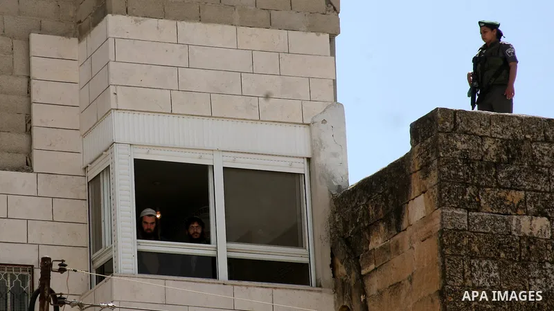 An Israeli settler looks out the window of an occupied Palestinian house as an Israeli soldier stands guard in the centre of Hebron in the occupied West Bank on March 29, 2012. Dozens of Jewish settlers took over the Pal...