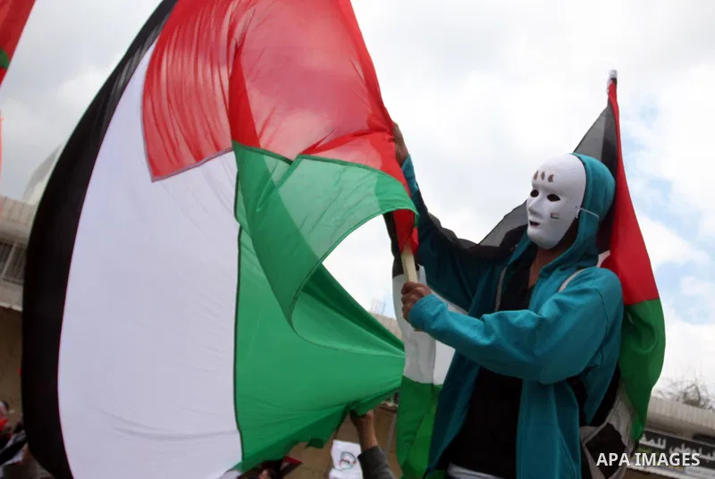 A masked Palestinian protester holds his national flag as he commemorates Land Day in Qalandia which lies between Jerusalem and the West Bank city of Ramallah on March 30, 2012. Land Day marks the annual event that comme...