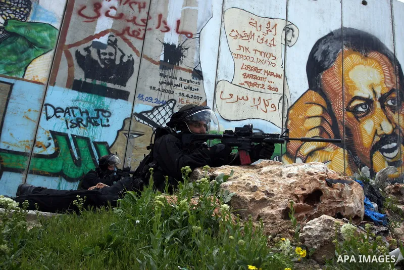 An Israeli soldier aims his rifle as Palestinians protesters mark the anniversary of Land Day in Qalandia which lies between Jerusalem and the West Bank city of Ramallah on March 30, 2012. Land Day marks the annual event...