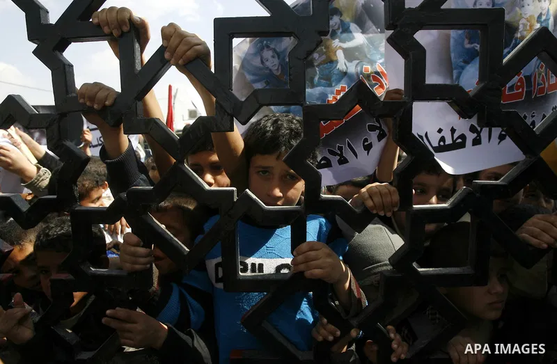 Palestinian boys hold a poster of three children who were killed in a fire caused by a candle being used due to lack of electricity during a protest against the electricity crisis near the southern Gaza Strip's Rafah bor...