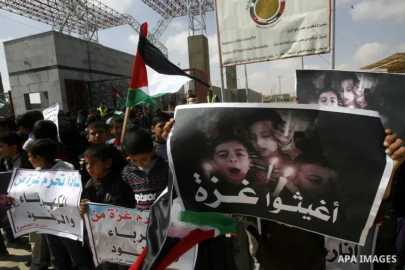 Palestinian boys hold a poster of children reading "Rescue Gaza" as another flashes the victory sign near the southern Gaza Strip's Rafah border crossing with Egypt on April 3, 2012 during a protest against the electrici...