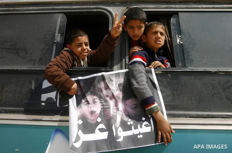 Palestinian boys hold a poster of children reading "Rescue Gaza" as another flashes the victory sign near the southern Gaza Strip's Rafah border crossing with Egypt on April 3, 2012 during a protest against the electrici...