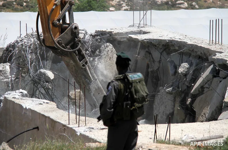 Israeli Border Police stand by as a security bulldozer demolishes a water storage tank owned by the Palestinians in the village of Dura, outside the West Bank city of Hebron, 16 April 2012. The reservoir building was dem...