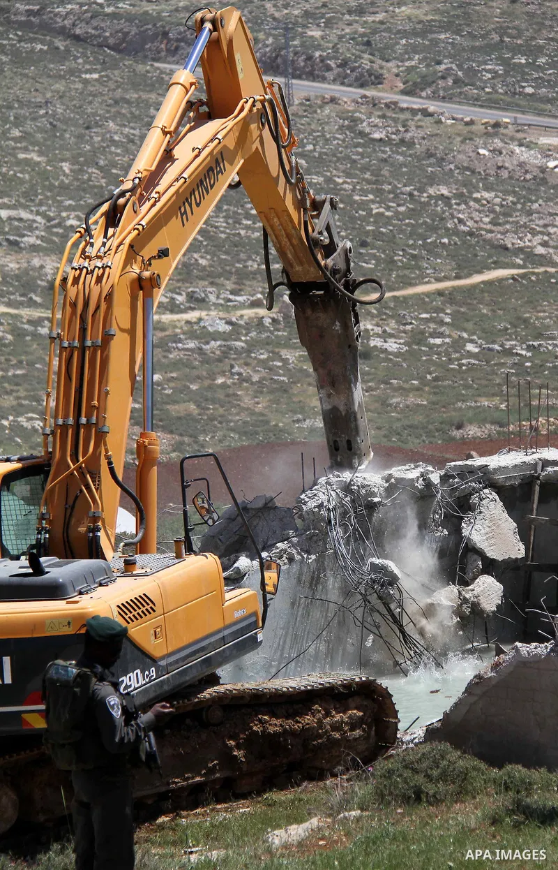 Israeli Border Police stand by as a security bulldozer demolishes a water storage tank owned by the Palestinians in the village of Dura, outside the West Bank city of Hebron, 16 April 2012. The reservoir building was dem...