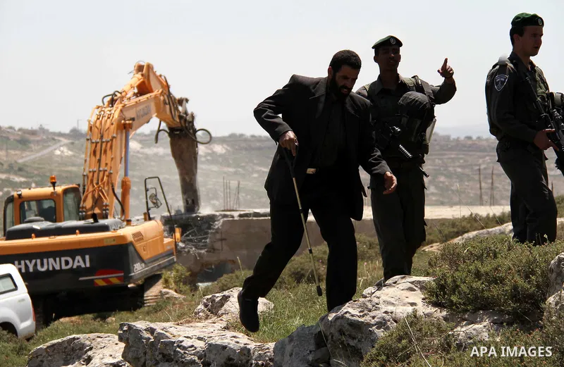 Israeli Border Police stand by as a security bulldozer demolishes a water storage tank owned by the Palestinians in the village of Dura, outside the West Bank city of Hebron, 16 April 2012. The reservoir building was dem...