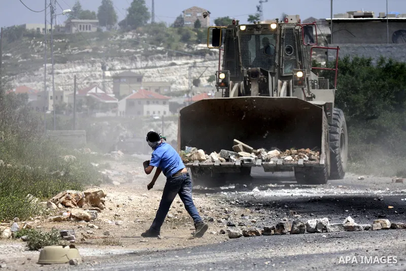 Palestinian protesters throws a stones at an Israeli military digger as it removes a barricade during a demonstration against the expropriation of Palestinian land by Israel in the village of Kafr Qaddum, near the northe...