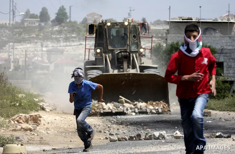 Palestinian protesters throws a stones at an Israeli military digger as it removes a barricade during a demonstration against the expropriation of Palestinian land by Israel in the village of Kafr Qaddum, near the northe...
