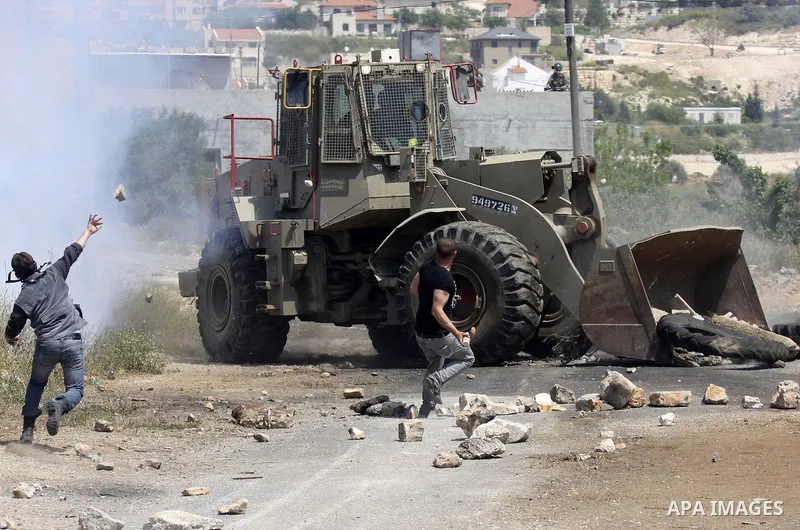 Palestinian protesters throws a stones at an Israeli military digger as it removes a barricade during a demonstration against the expropriation of Palestinian land by Israel in the village of Kafr Qaddum, near the northe...