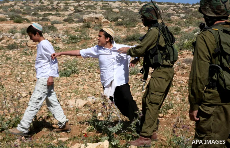 Israeli Jewish settlers look on as Israeli soldiers move Palestinian farmers and shepherds off their land to allow the settlers to farm the land near the Maaon Jewish settlement, just south of the Palestinian village of...