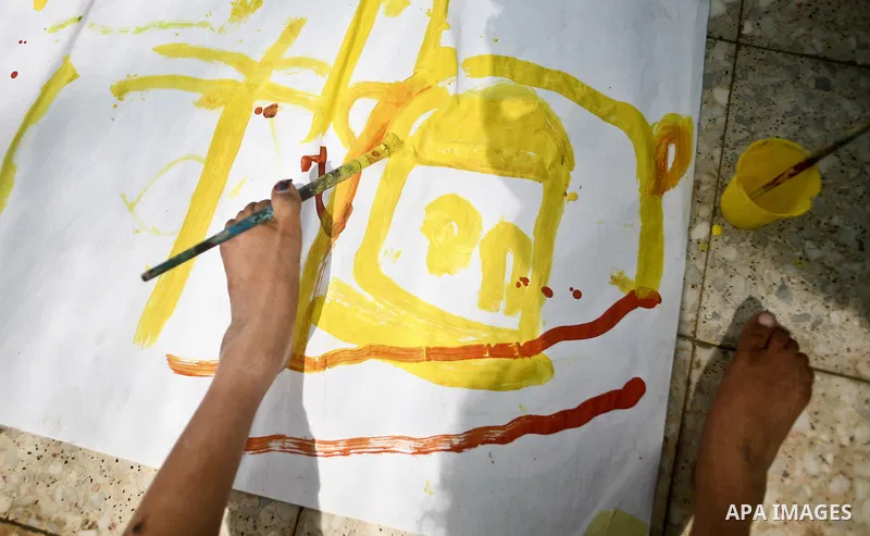 A Palestinian disabled child uses his feet to draw and paint pictures at a charity association during a celebration in Gaza city on April 23,2012. Photo by Ali Jadallah