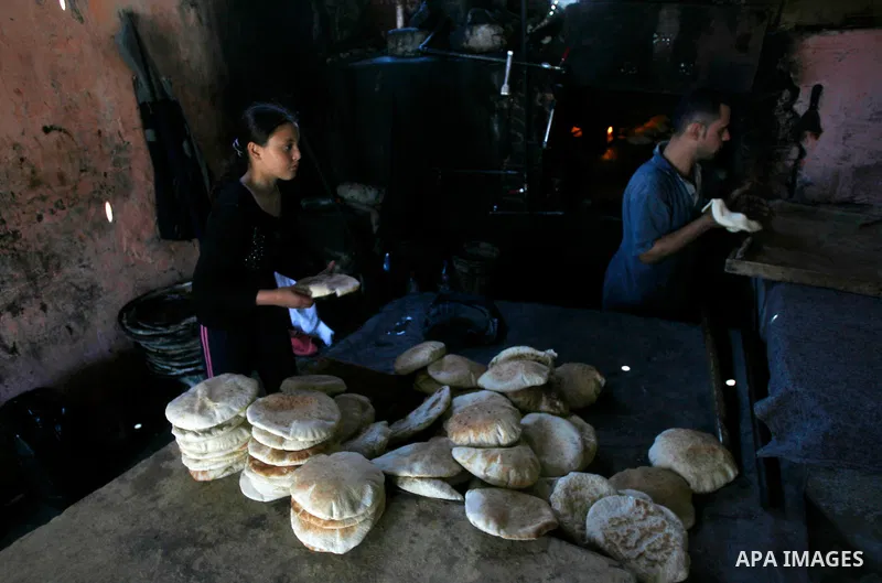 A Palestinian girl helps baker to bake loaves of bread in a traditional mud oven in Rafah refugee camp, southern Gaza Strip on April 28, 2012. Photo by Eyad Al Baba