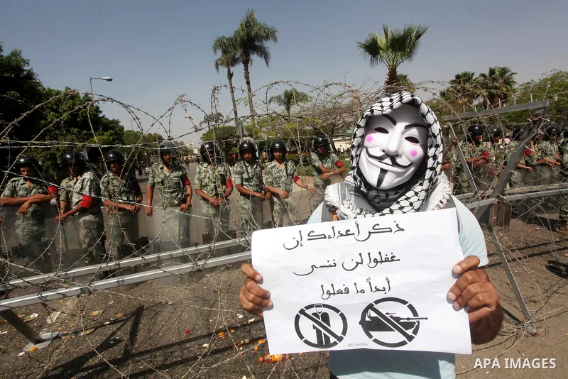 An Egyptian protester wearing a Guy Fawkes mask holds a sign reading "Remind your enemies that we will never forget what they have done" during a demonstartion against the interim military leadership outside the defence...