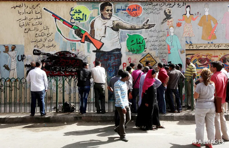 Egyptian people stand in front of graffiti on a wall in Tahrir Square in Cairo on May 01, 2012. Egyptians demanded that their military rulers pledge to hand over power by mid-year after a row over who can run in the pres...