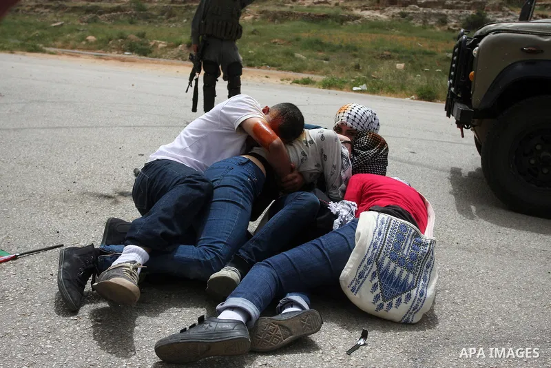 Palestinian protesters who were hit with pepper spray by Israeli border police, lie on the ground as they try to prevent Israeli troops from detaining one of them, during clashes outside Ofer prison near the West Bank ci...