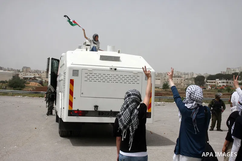 A Palestinian woman, her hair covered by white keffiyeh, waves a national flag as she stands atop an Israeli military vehicle during a protest by some 300 people gathered outside Ofer military prison near the West Bank c...