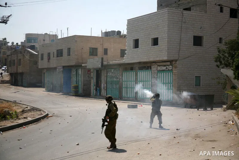 Palestinian protesters run for cover from the teargas fired by Israeli soldiers during clashes broke out in the village of Beit Ommar, near the northern West Bank city of Hebron, following a demonstration solidarity with...