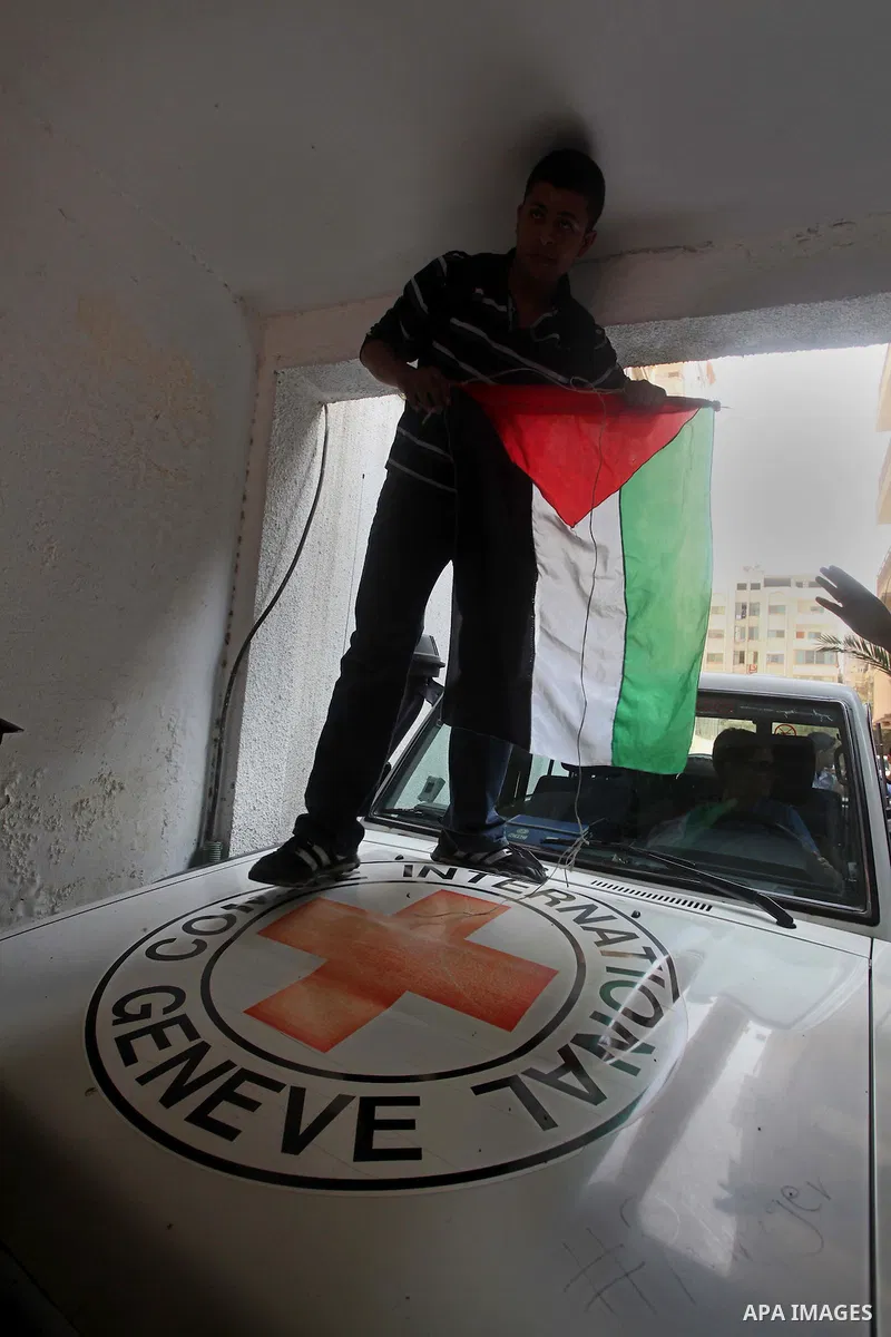 A Palestinian man holding a Palestinian flag stands on top of an International Committee of the Red Cross (ICRC) vehicle in Gaza as protestors forced the offices to close for two hours in solidarity with over 1,550 priso...