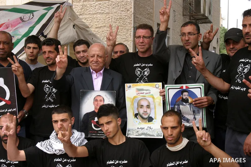 Palestinian chief negotiator Ahmed Qorei (C) holds a picture of a Palestinian prisoner and flashes the sign for victory during his visit to a protest tent outside the International Committee of the Red Cross (ICRC) offic...