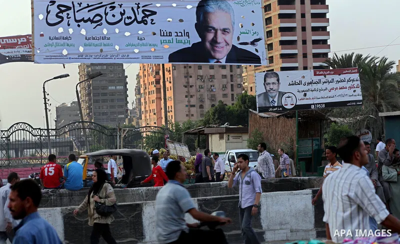 Egyptians walk behind an election campaign banner for the presidential candidate, Hamdin Sabahi, in Cairo on May 21, 2012. The Supreme Council of the Armed Forces urged Egyptians to accept the results of a looming presid...