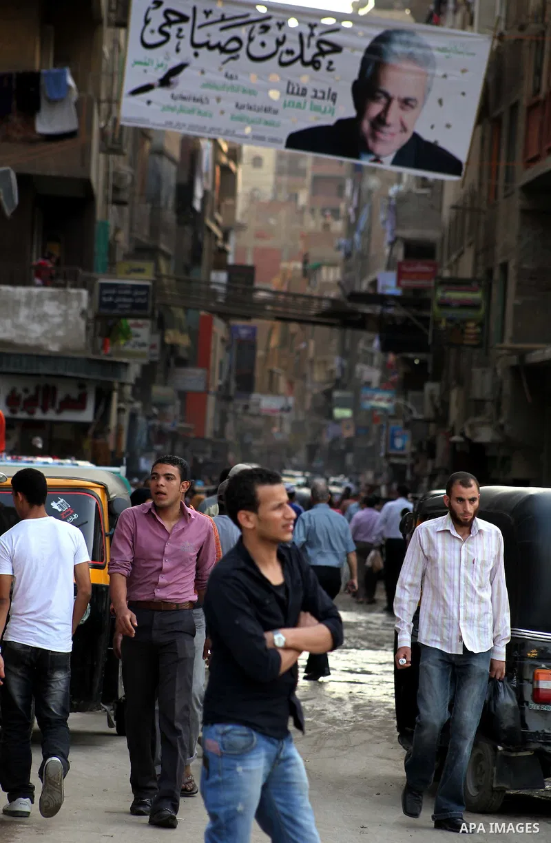 Egyptians walk behind an election campaign banner for the presidential candidate, Hamdin Sabahi, in Cairo on May 21, 2012. The Supreme Council of the Armed Forces urged Egyptians to accept the results of a looming presid...