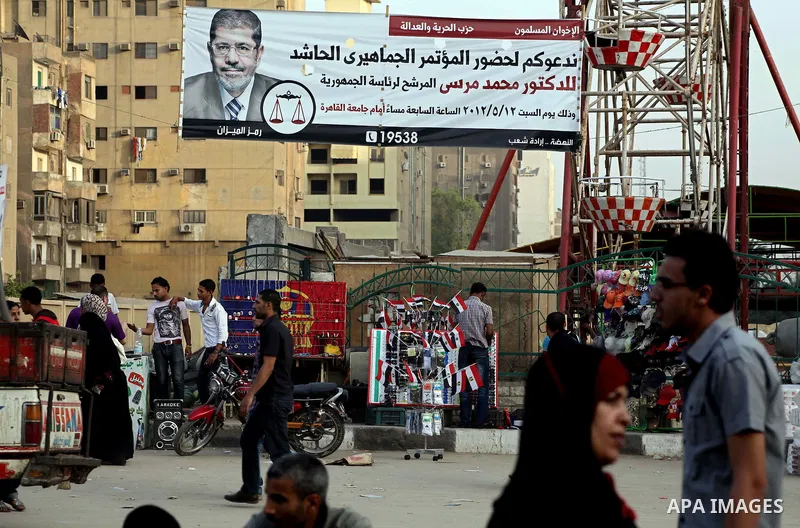 Egyptians walk behind an election campaign banner for the Muslim Brotherhood's presidential candidate, Mohammed Mursi, in Cairo on May 21, 2012. The Supreme Council of the Armed Forces urged Egyptians to accept the resul...
