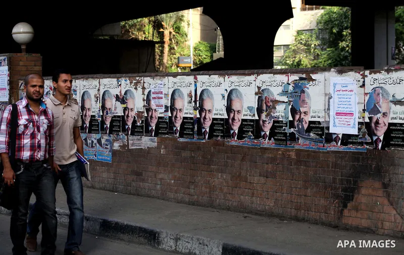 Egyptians walk behind an election campaign banner for the presidential candidate, Hamdin Sabahi, in Cairo on May 21, 2012. The Supreme Council of the Armed Forces urged Egyptians to accept the results of a looming presid...