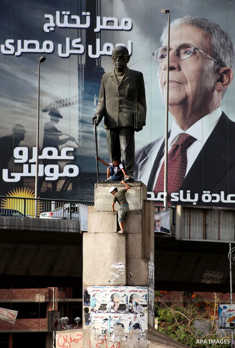 Egyptian boys sit underneath a statue of Egyptian novelist Naguib Mahfouz seen in front of a huge election campaign banner for former foreign minister and Arab League chief and presidential candidate, Amr Mussa, in Cairo...