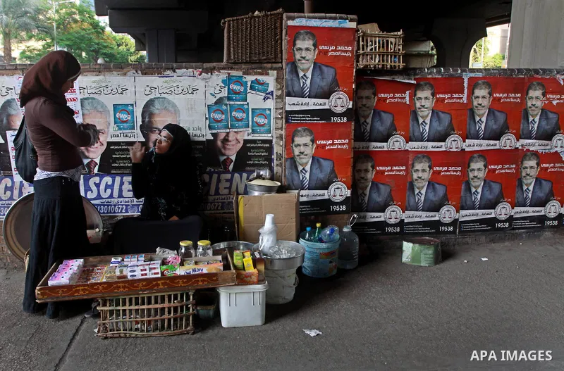An Egyptian woman seller sits in front of election campaign posters for the Muslim Brotherhood's presidential candidate, Mohammed Mursi, in Cairo on May 21, 2012. The Supreme Council of the Armed Forces urged Egyptians t...
