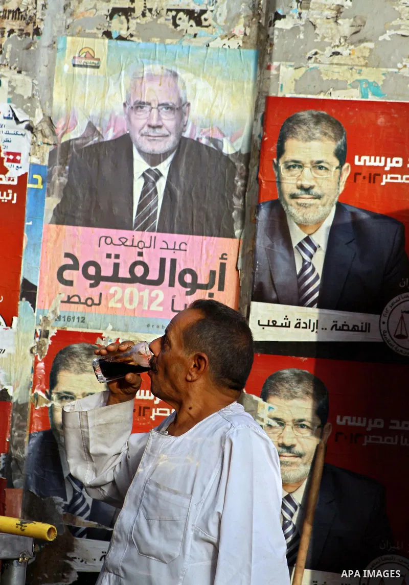An Egyptian man drinks in front of election campaign posters for the Muslim Brotherhood's presidential candidate, Mohammed Mursi, in Cairo on May 21, 2012. The Supreme Council of the Armed Forces urged Egyptians to accep...