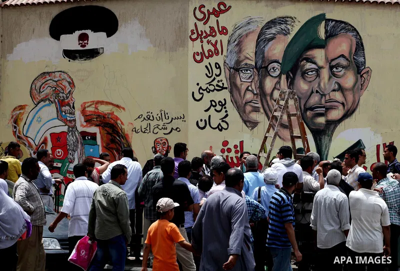 An artist writes a slogan in Arabic that reads "I will never give you peace" next to a graffiti picturing the morphed faces of ousted president Hosni Mubarak (R) and military ruler Hussein Tantawi and presidential candid...