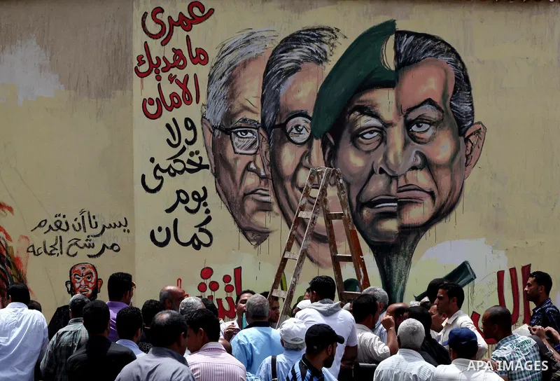 An artist writes a slogan in Arabic that reads "I will never give you peace" next to a graffiti picturing the morphed faces of ousted president Hosni Mubarak (R) and military ruler Hussein Tantawi and presidential candid...