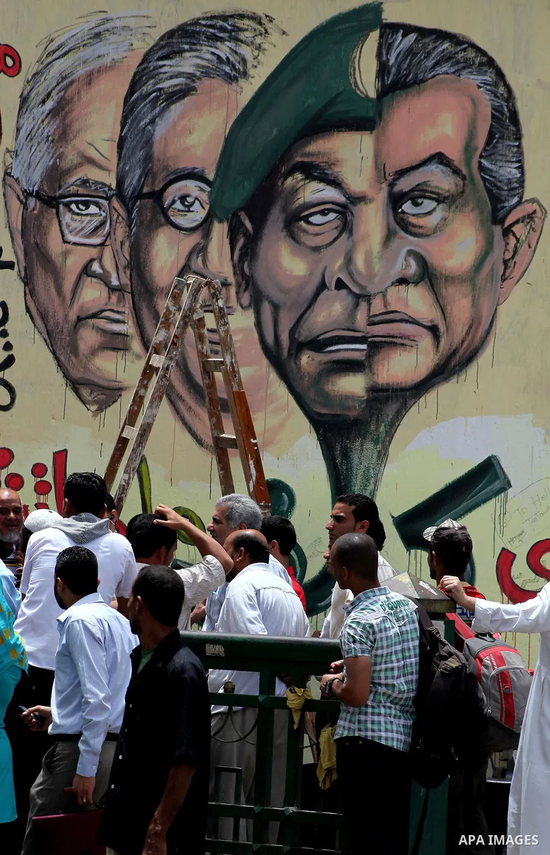 An artist writes a slogan in Arabic that reads "I will never give you peace" next to a graffiti picturing the morphed faces of ousted president Hosni Mubarak (R) and military ruler Hussein Tantawi and presidential candid...