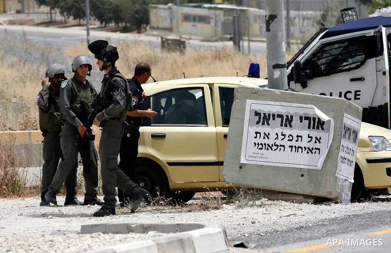 Israeli soldiers look at a blindfolded and handcuffed Palestinian youth, as he sits in the back of a car after he was arrested at the Hawara checkpoint on the southern edge of the northern Palestinian city of Nablus in t...