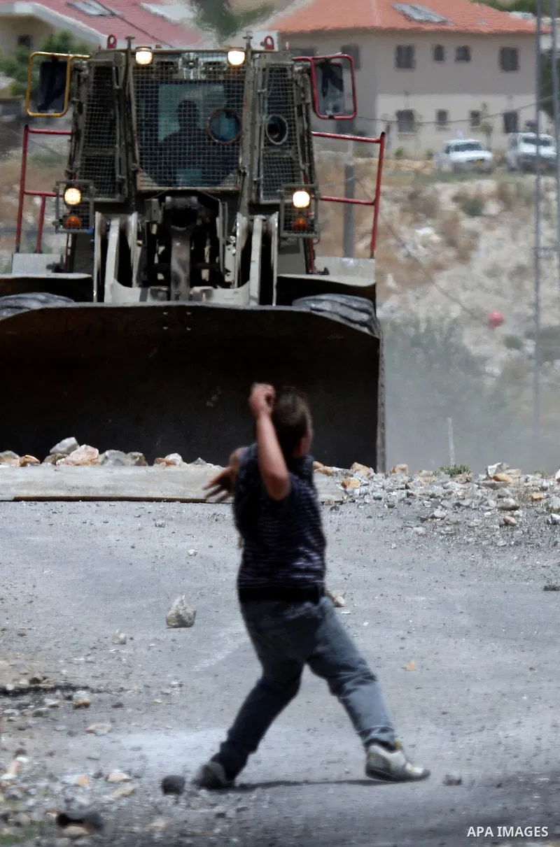 A Palestinian protester throws stone at an Israeli army bulldozer during clashes in the northern West Bank village of Kufr Qaddum, near the Jewish settlement of Kdumim, on May 25, 2012. Photo by Wagdi Eshtayah